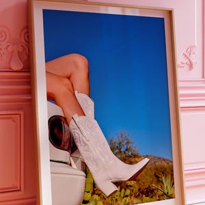 May include: A framed poster with the text "SUBTLE MUSIC POSTERS" at the top. The poster features a photograph of white cowboy boots and legs against a blue sky and desert landscape. The text "COWBOY LIKE ME" and "VOLUME 09 NO 11" are at the bottom.