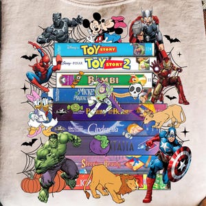 May include: A beige sweatshirt with a design of stacked Disney VHS tapes, including 'Toy Story' and 'Cinderella', with characters like Spider-Man and Hulk. The design incorporates Halloween elements such as bats and pumpkins.