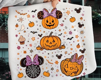 May include: White Halloween-themed towel featuring orange jack-o'-lanterns, bats, stars, and Mickey Mouse-inspired pumpkins with purple bows. The design includes a ghost, cupcake, and spiderwebs, creating a festive and spooky atmosphere.