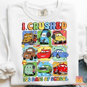May include: White sweatshirt with a colorful graphic featuring cartoon cars and the text "I CRUSHED 100 DAYS OF SCHOOL." The design includes various car characters in different colors and styles, perfect for a school celebration.
