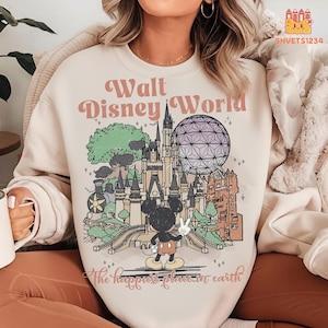 Puede incluir: Sudadera color crema con un diseño de Walt Disney World con Mickey Mouse, un castillo y Spaceship Earth. El diseño incluye el texto "Walt Disney World" y "the happiest place on earth" en rosa y marrón.