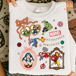 May include: White sweatshirt with Marvel comic book characters such as Captain America, Iron Man, and Wonder Woman. The design includes the word "Marvel" and the phrase "May the Force Be With You".