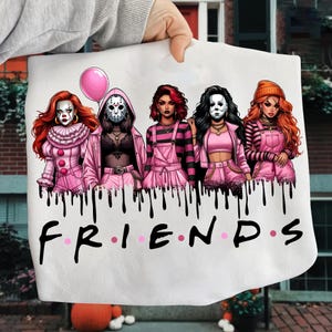May include: White graphic tee featuring five stylized horror characters in pink outfits, with a pink balloon. The word "FRIENDS" is written in black with pink dots. Black drips are at the top of the word.
