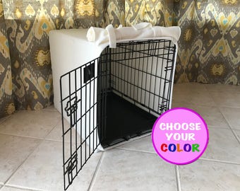 May include: A black wire pet crate featuring a white fabric cover draped over the top and sides. The crate has an open front door and a black plastic floor tray. A circular pink graphic overlay in the bottom right corner displays the text CHOOSE YOUR COLOR.