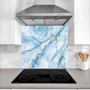 May include: A blue and gold marble-effect kitchen splashback. The design has a watercolour effect with shades of blue and gold accents. The splashback is installed behind a black electric hob and beneath a stainless steel cooker hood.