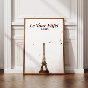 May include: A framed print featuring the Eiffel Tower in Paris, France. The brown wooden frame surrounds a white background with the tower and the words "Le Tour Eiffel PARIS" in brown. Silhouettes of birds are scattered across the sky.