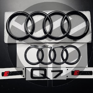 Könnte beinhalten: Schwarzes Audi-Ringemblem mit dem Text "Q7" in Schwarz auf weißem Hintergrund. Das Emblem befindet sich auf einer weißen Oberfläche.