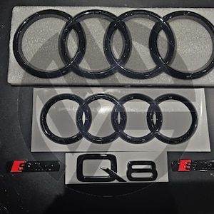 May include: Black and white Audi car emblem with four interlocking rings. The emblem is on a white background with the text "Q8" in black below it.