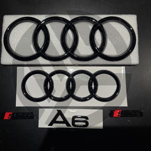 May include: Black Audi emblem with four interlocking rings, a smaller black Audi emblem with four interlocking rings, and a black emblem with the text "A6" in white.