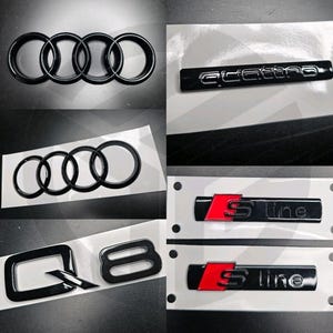 May include: A collection of black car emblems, including the Audi four-ring logo, "quattro" badge, "S line" badges with red accents, and a "Q8" emblem. The emblems are displayed on a white background.