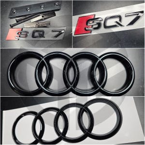 Puede incluir: Colección de emblemas y piezas de automóviles, incluyendo el logotipo SQ7 en plata y rojo, y el icónico emblema de cuatro anillos en negro. También se ven componentes de hardware.