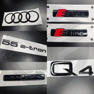 Może przedstawiać: Zestaw czarnych i czerwonych emblematów samochodowych. Emblematy obejmują pierścienie Audi, "S line", "Q4", "55 e-tron" i "quattro".