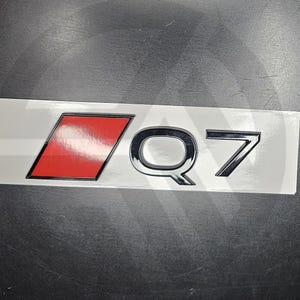 Puede incluir: Una pegatina rectangular blanca con un cuadrado rojo y letras negras que dicen "Q7".