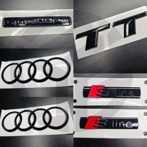 Puede incluir: Una colección de emblemas y logotipos de coches negros, incluyendo "Quattro", "TT", los anillos de Audi y distintivos "S line" con detalles rojos. Los emblemas están sobre un fondo blanco.