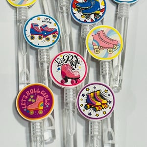 Può includere: Una collezione di bacchette per bolle di sapone in plastica trasparente con disegni di pattini a rotelle colorati. Ogni bacchetta presenta un design di pattino a rotelle in colori come rosa, blu e giallo, con testi come "Let's Roll Girls" e "Let's Have Fun!"