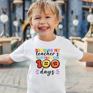 May include: White t-shirt with a colorful graphic that says "Pushing my teacher's buttons for 100 days". The graphic features colorful buttons with a rainbow design.