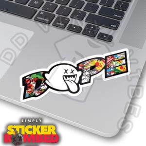 Könnte beinhalten: Ein weißer Aufkleber mit dem Wort "DOPE" im Graffiti-Stil, der einen Cartoon-Geist-Charakter zeigt. Der Aufkleber hat einen schwarzen Rand und befindet sich auf einem Laptop. Der Geist hat durchgestrichene Augen und eine lange Zunge. Der Aufkleber ist von "SIMPLY STICKER BOMBED".