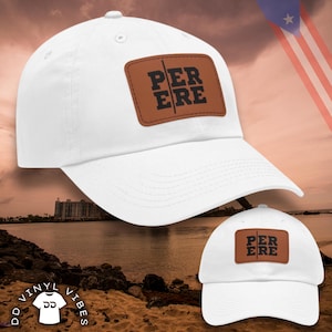 May include: White baseball cap with a brown leather patch featuring the text "PER ERE" in black. The cap is displayed against a beach scene with a flag in the background. The cap is a classic style with a curved brim.