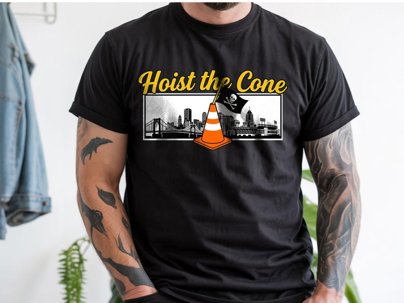 May include: Black t-shirt with the text "Hoist the Cone" in yellow. The design features a traffic cone with a pirate flag and a cityscape. The shirt is a crew neck and short-sleeved.