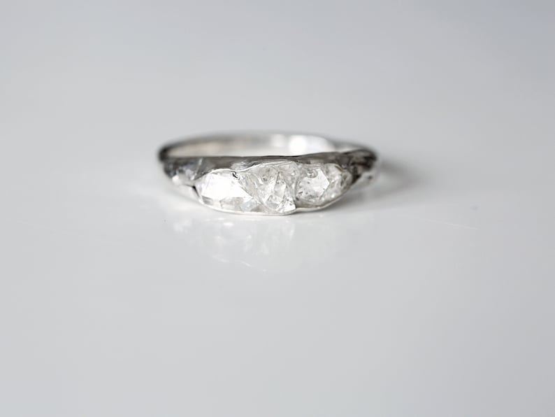 May include: A silver ring with three large, clear, faceted stones set in a textured band.
