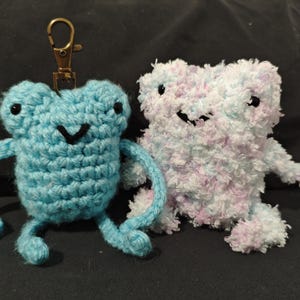 May include: Two crocheted plush toys, one blue frog with a key chain and one white and purple fluffy creature.