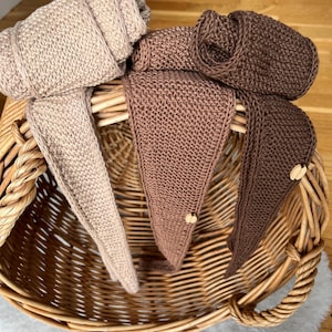 Könnte beinhalten: Drei dreieckige Strickstirnbänder in den Farben Beige, Hellbraun und Dunkelbraun. Jedes Stirnband weist ein strukturiertes Strickmuster auf und ist mit einem kleinen, runden, hellen Holzknopf am spitzen Ende des Stoffes versehen.