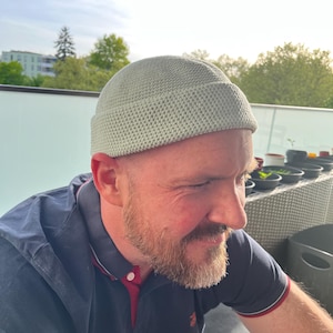Könnte beinhalten: Eine hell salbeigrüne Beanie-Mütze mit einem engen, gleichmäßigen Häkelmuster und einem umgeschlagenen Rand. Die Mütze hat eine abgerundete Krone und eine strukturierte, kreisförmige Form, die fest auf dem Kopf sitzt und eine Textur zeigt.