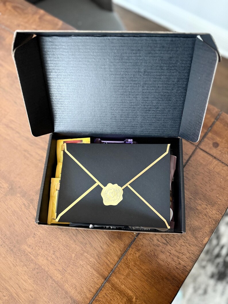 May include: A black box containing a gold envelope. The envelope has a gold wax seal with a design on it.