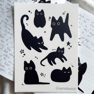 May include: A sticker sheet featuring black cat illustrations in various poses, with star accents. The sticker sheet is on a white background, with the text "October 2025" visible in the background.