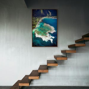 Aerial photograph of Kauai Hawaii coastline near Na Pali Coast showing turquoise ocean reef, shore break waves, and lush green mountains at sunset. Captured from helicopter, detailed ocean floor visible with vibrant tropical water and beach shoreline.