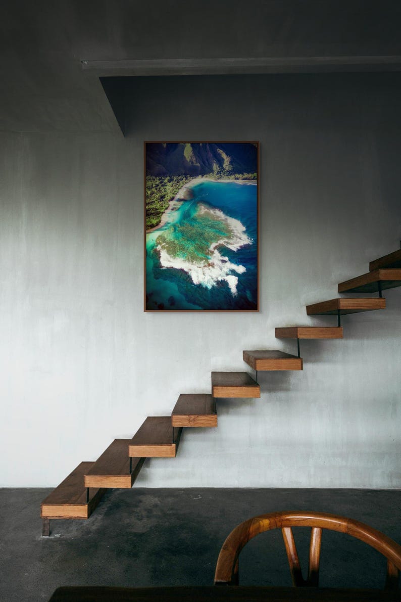Aerial photograph of Kauai Hawaii coastline near Na Pali Coast showing turquoise ocean reef, shore break waves, and lush green mountains at sunset. Captured from helicopter, detailed ocean floor visible with vibrant tropical water and beach shoreline.