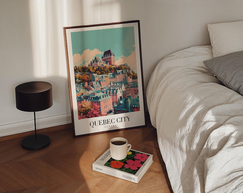May include: A vintage-style poster with a colorful illustration of the cityscape of Quebec City, Canada. The poster is framed and hanging on a white wall above a bed with white linens.
