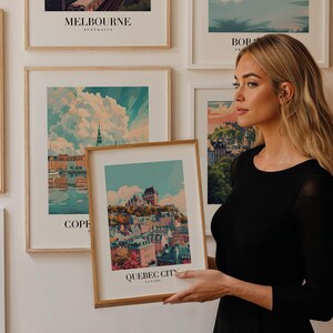 May include: A woman holds a framed print of a city skyline with the text "QUEBEC CITY CANADA". The print is surrounded by other framed prints of cityscapes.