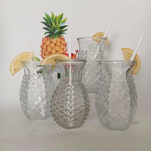 May include: Four clear, pineapple-shaped drinking glasses with white straws and lemon slices. The glasses have a diamond pattern. A pineapple illustration is in the background.