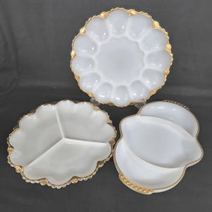 Peut inclure: Trois plats de service blancs avec des bordures dorées. Les plats comprennent une assiette divisée, une assiette festonnée avec des indentations en forme d'œuf et un plat à deux sections. Les bordures dorées ajoutent une touche d'élégance.