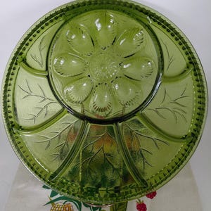 May include: A vintage green glass serving platter with a floral and leaf design. The round platter has multiple compartments and a decorative edge. The centre features a flower-like pattern, and the outer sections have leaf motifs.