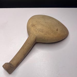 May include: A wooden spoon with a rounded bowl and a long handle. The spoon is made of light-colored wood and has a simple, rustic design. The handle ends in a rectangular shape.