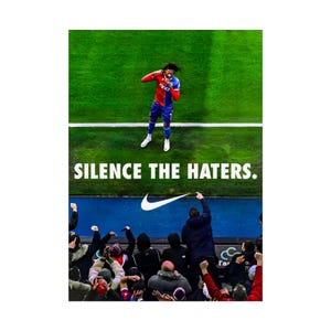 以下が含まれることがあります： 緑のフィールドで祝う赤と青のユニフォームを着たサッカー選手をフィーチャーしたプロモーション画像。「SILENCE THE HATERS」というテキストが選手の真下に表示され、ナイキのスウッシュロゴが付いています。背景にはファンの群衆が見えます。