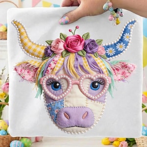 May include: A white square fabric with a colorful, whimsical cow face design. The cow has heart-shaped glasses, floral horns, and a flower crown. The design incorporates various patterns and textures, including gingham, floral prints, and pearls.