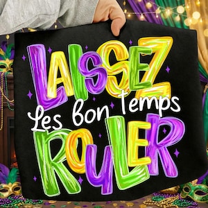May include: Black tote bag with the words "Laissez les bon temps rouler" in colorful, 3D lettering. The text is in purple, yellow, green, and orange, with small purple star accents. The bag is held up by a person.