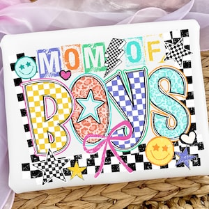 May include: White rectangular item with the text "MOM OF BOYS" in colorful, patterned letters. The design includes stars, hearts, a lightning bolt, and a bow, all set against a black and white checkered border.