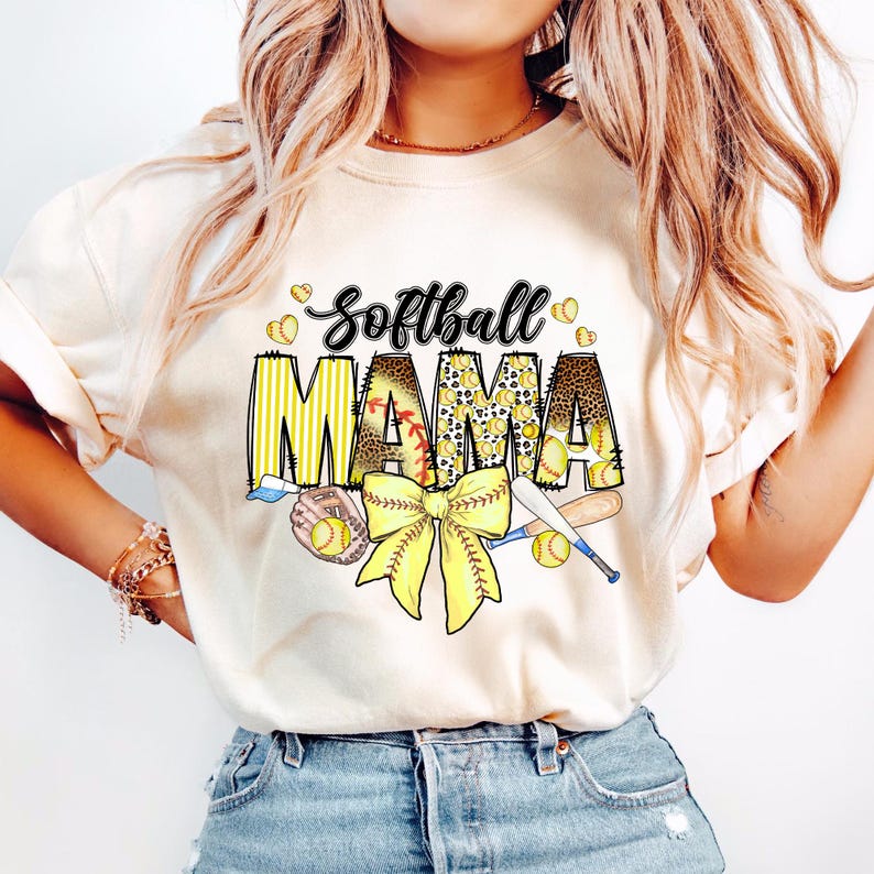 May include: A white t-shirt with the text "Softball Mama" in black and yellow lettering. The text is surrounded by a yellow and black leopard print design, a yellow bow, and baseballs.