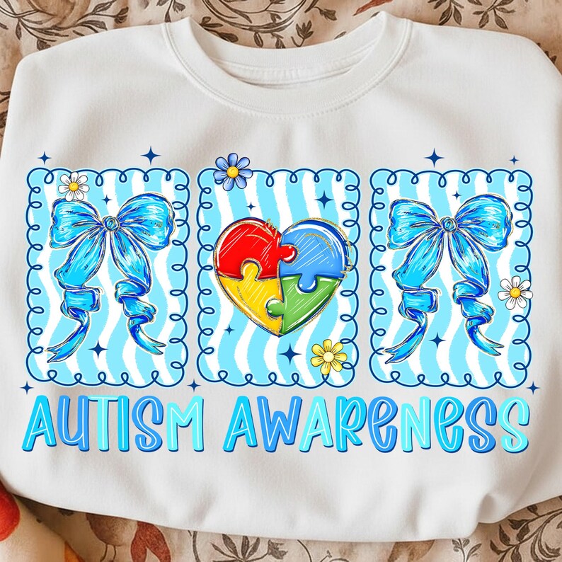 May include: White sweatshirt with a blue and white design promoting autism awareness. The design includes blue bows, a puzzle heart, and the words "AUTISM AWARENESS" in blue letters. The design is framed with a blue border.