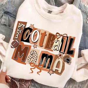 May include: White sweatshirt with the words "Football Mama" in a collage style design. The design includes a football, stars, a helmet, and bows in shades of brown, black, and tan.
