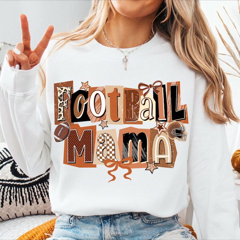 May include: White sweatshirt with the text "Football Mama" in a collage style. The text features various patterns, including leopard print, gingham, and solid colors. A football, stars, and a helmet are also included in the design.