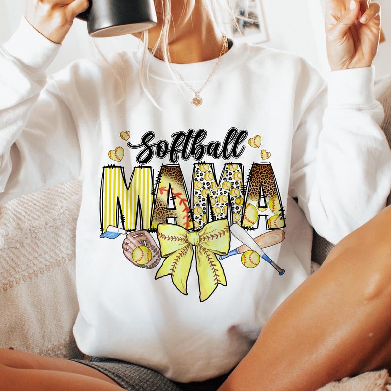 May include: White sweatshirt with the text "Softball Mama" in yellow and black letters with a yellow bow, baseballs, and bats.