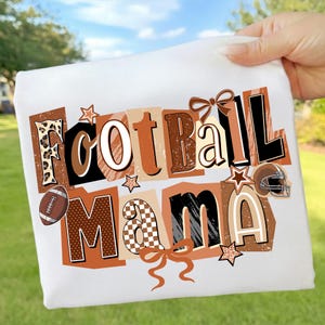May include: White t-shirt with the words "Football Mama" in a collage of brown, black, and tan letters. The design includes a football, stars, a helmet, and bows. The shirt is held up against a background of green grass and a blue sky.