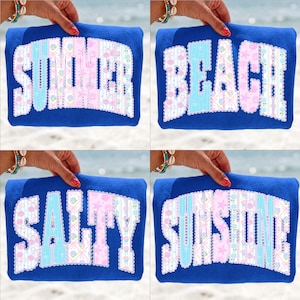 May include: Four blue rectangular pillows with white text. The pillows say "SUMMER", "BEACH", "SALTY", and "SUNSHINE". The text is in a playful font with a floral and geometric pattern in pink and blue.