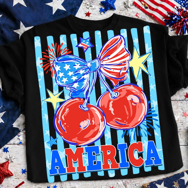 May include: Black t-shirt featuring a patriotic design with red cherries, a blue bow, and the word "AMERICA" in blue and red. The design includes stars and stripes, celebrating American Independence.