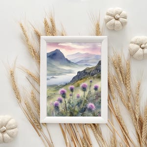 以下が含まれることがあります： 湖を前景に描いた山岳風景の水彩画。絵は白い額縁に収められており、前景に紫色の花が描かれている。